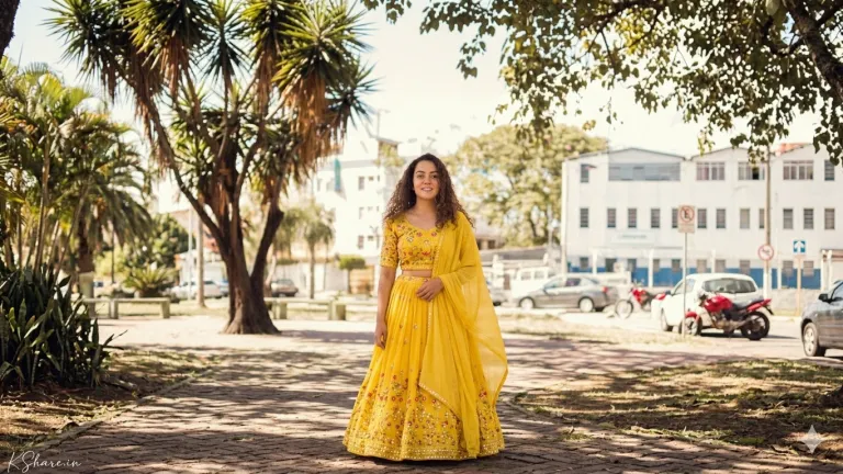 A second pose of the young woman in the identical yellow and gold lehenga choli seen in image_17.png. Her stance is similar, but the way she holds the sheer net dupatta has changed, draping it over her right arm and slightly to her side, with her right hand visible. The outfit details, gold embroidery, and mirror work are preserved. A second pose of the young woman in the identical yellow and gold lehenga choli seen in image_17.png. Her stance is similar, but the way she holds the sheer net dupatta has changed, draping it over her right arm and slightly to her side, with her right hand visible. The outfit details, gold embroidery, and mirror work are preserved.